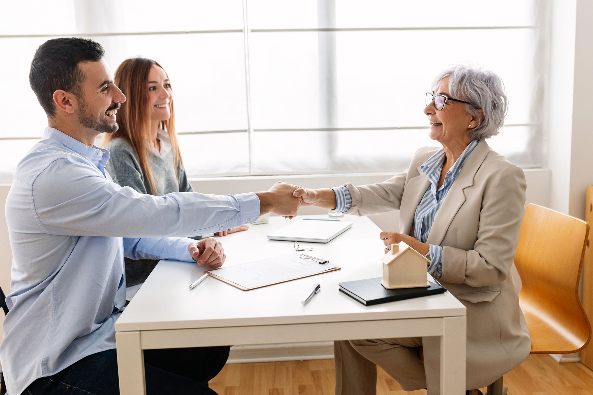 Client and agent shaking hands after finalizing public insurance payout agreement at office desk.