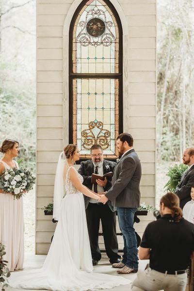 Wedding couple exchanging vows before officiant in a bright chapel with stained glass window