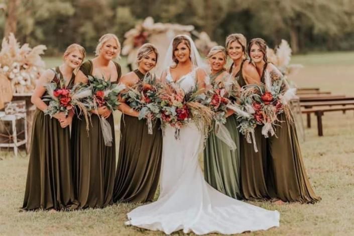 Bridal party posing outdoors, bride in white gown with bridesmaids in olive dresses holding bouquets