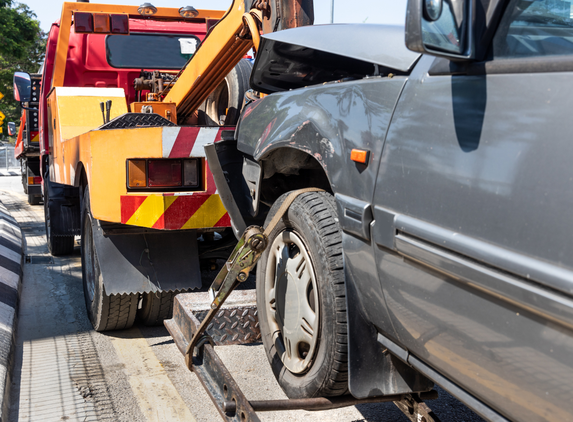 A tow truck is towing a damaged car on the side of the road.