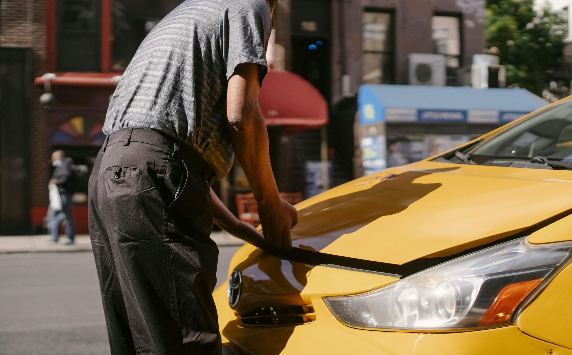 A man is standing next to a yellow taxi with the hood open.