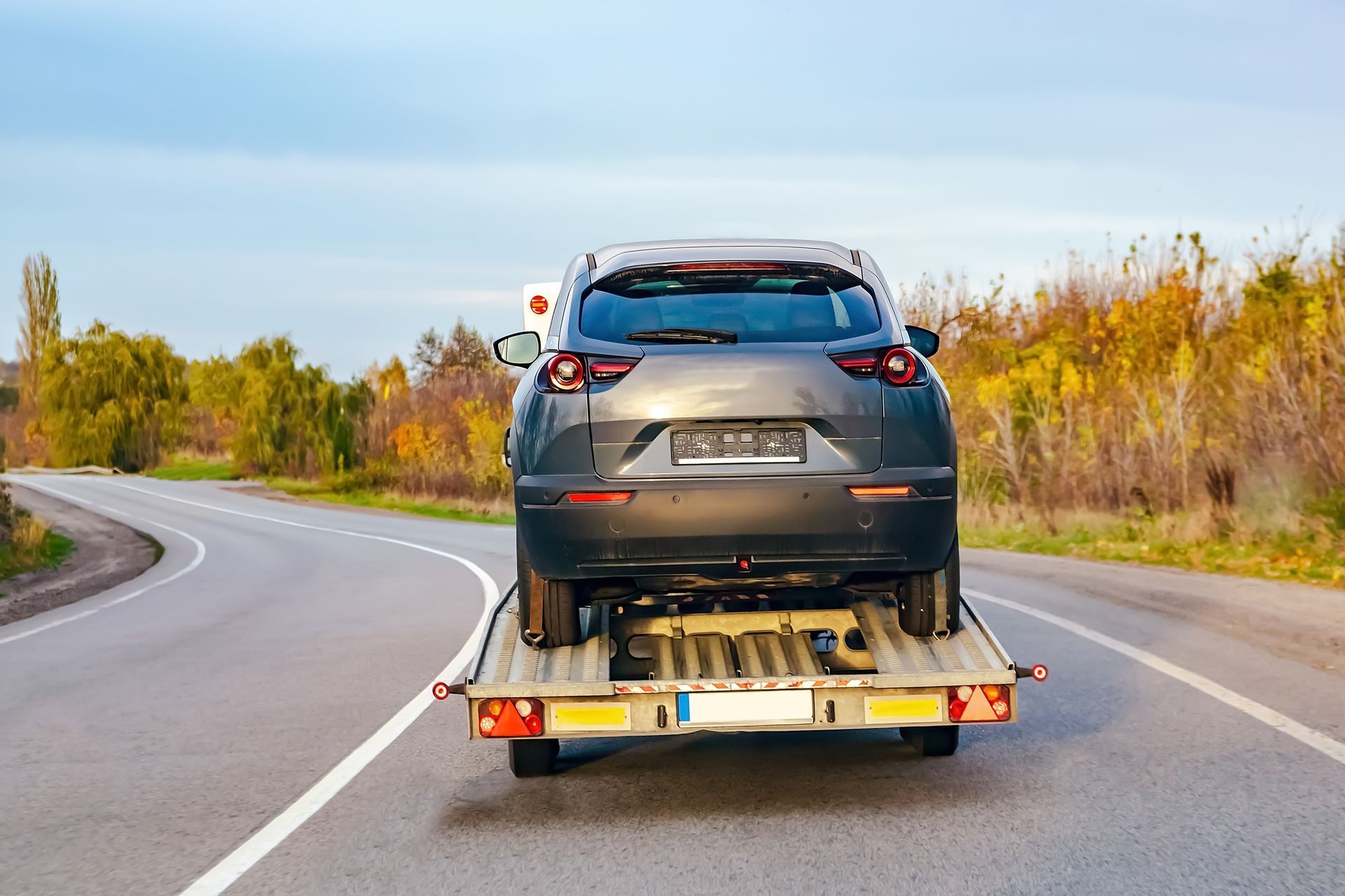 A car is being towed down a road by a tow truck.