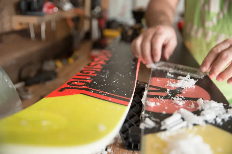 A person is waxing a snowboard in a workshop.