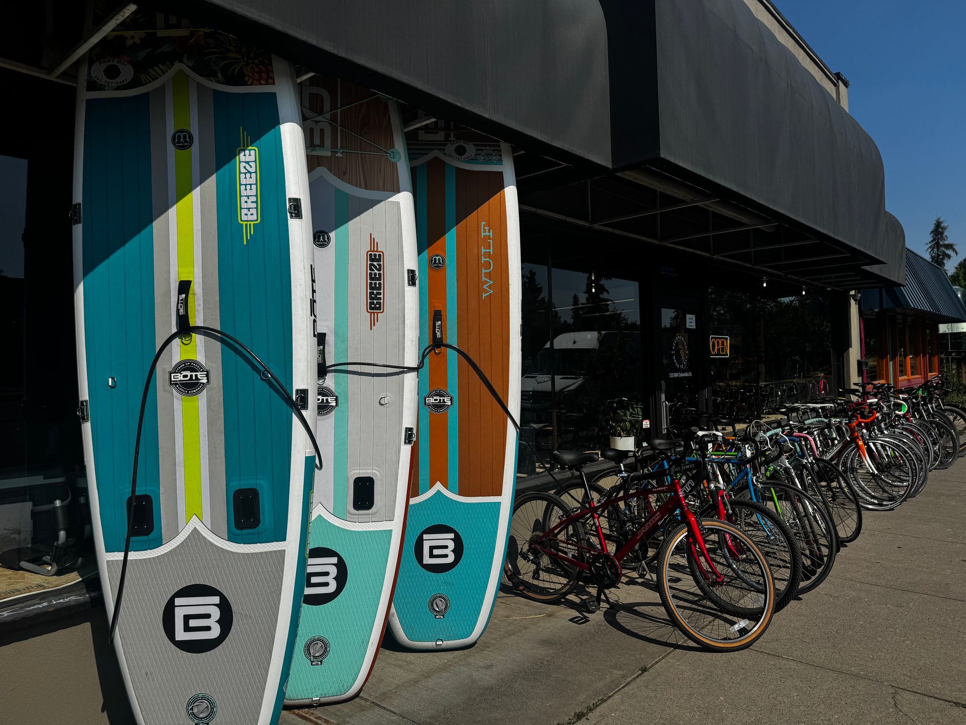 Stand-up paddleboards and bicycles displayed outside a store on a sunny day.
