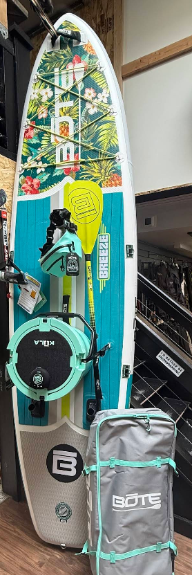 A surfboard is sitting on a wooden floor next to a bag.