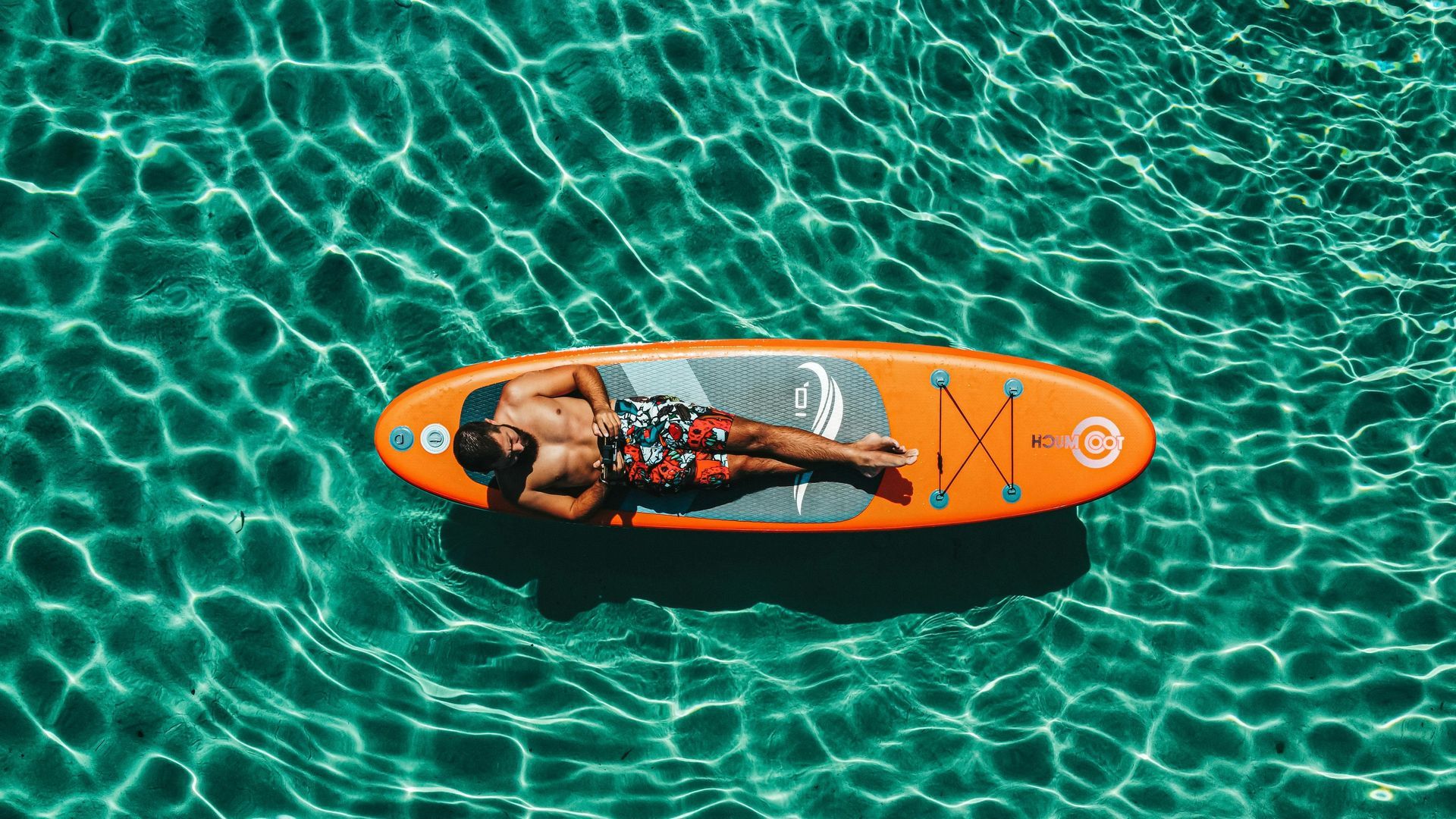 Man relaxing on an orange paddleboard in clear turquoise water.