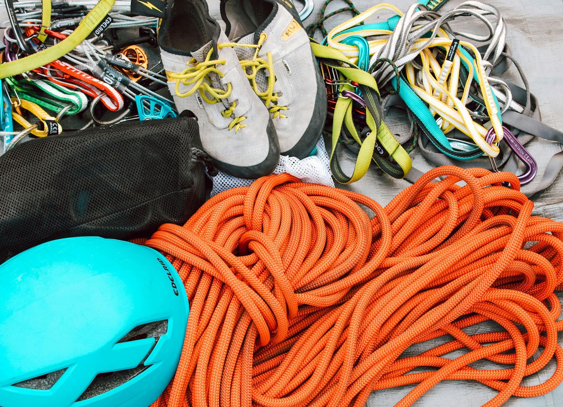 A bright blue climbing helmet, orange climbing rope, light gray climbing shoes, and assorted carabiners and gear slings.