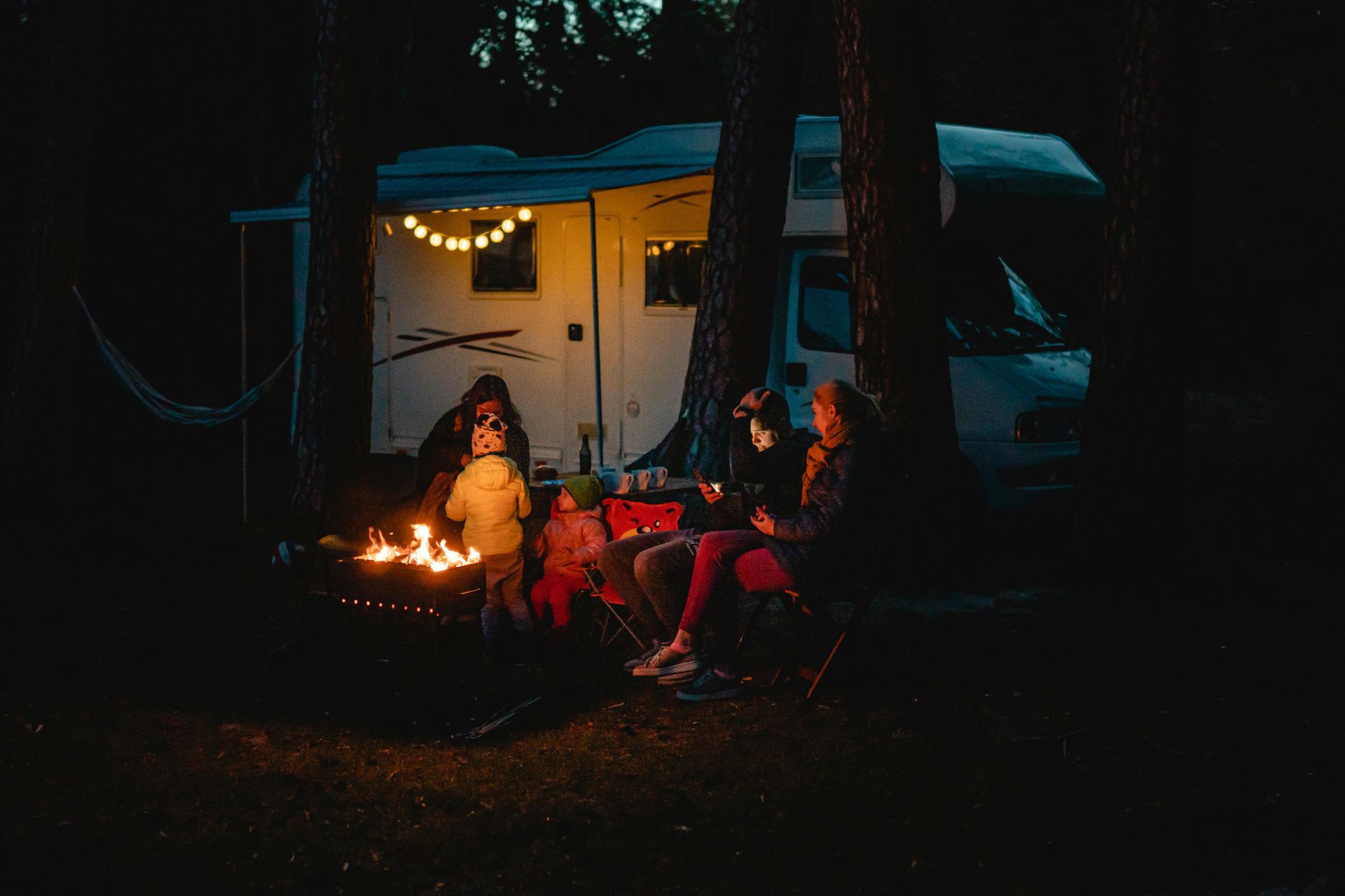People gathered around a campfire outside a glowing tent at night in a wooded campsite