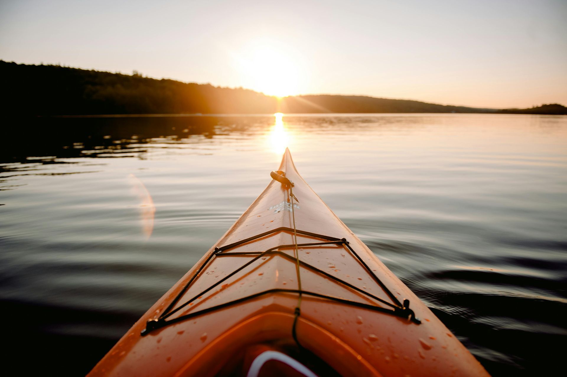 Orange kayak on calm lake at sunrise, facing the glowing horizon.