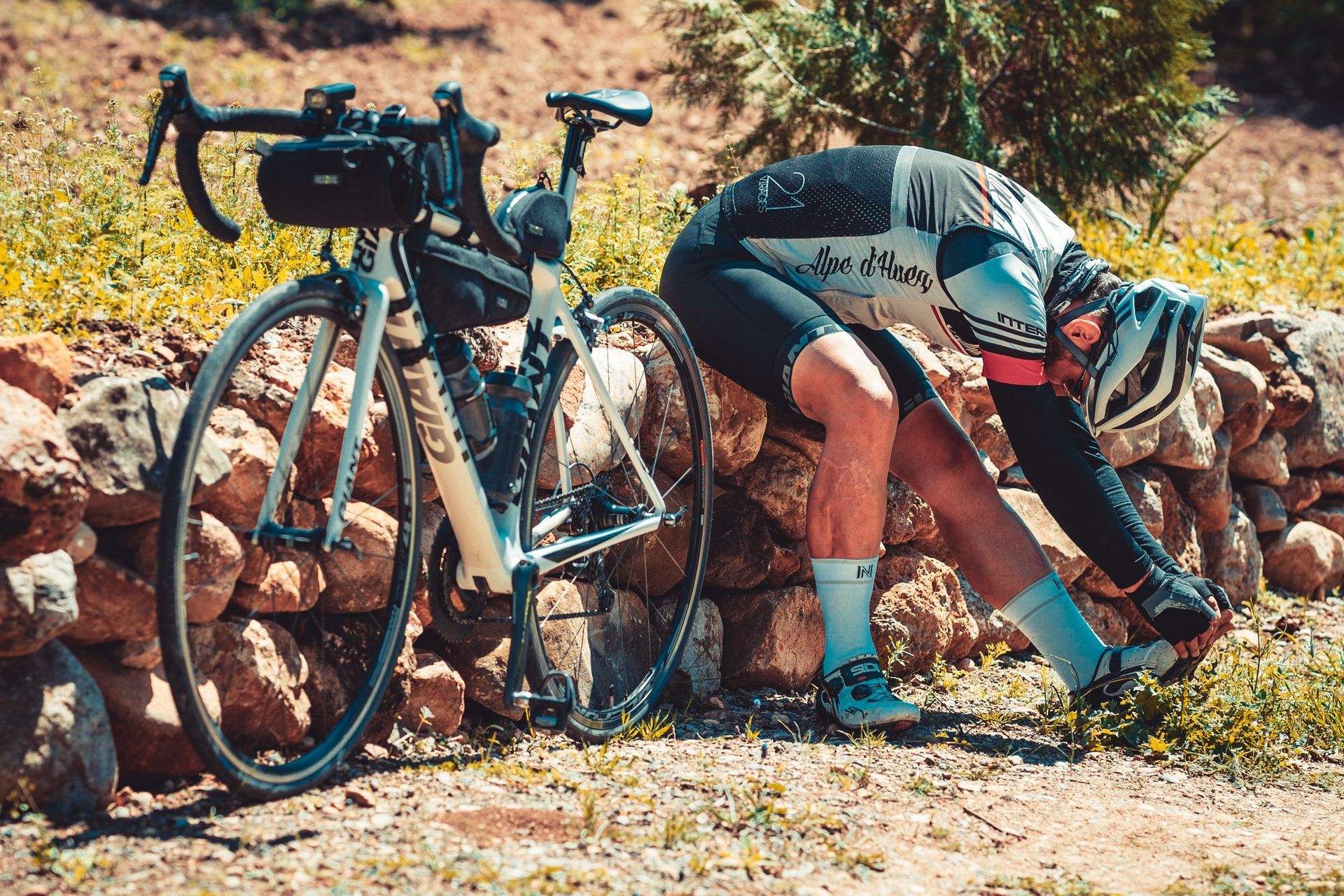 Cyclist fixing a bike beside two road bikes on a rocky trail in sunny countryside