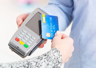 Person holding a blue credit card near a payment terminal for contactless payment.