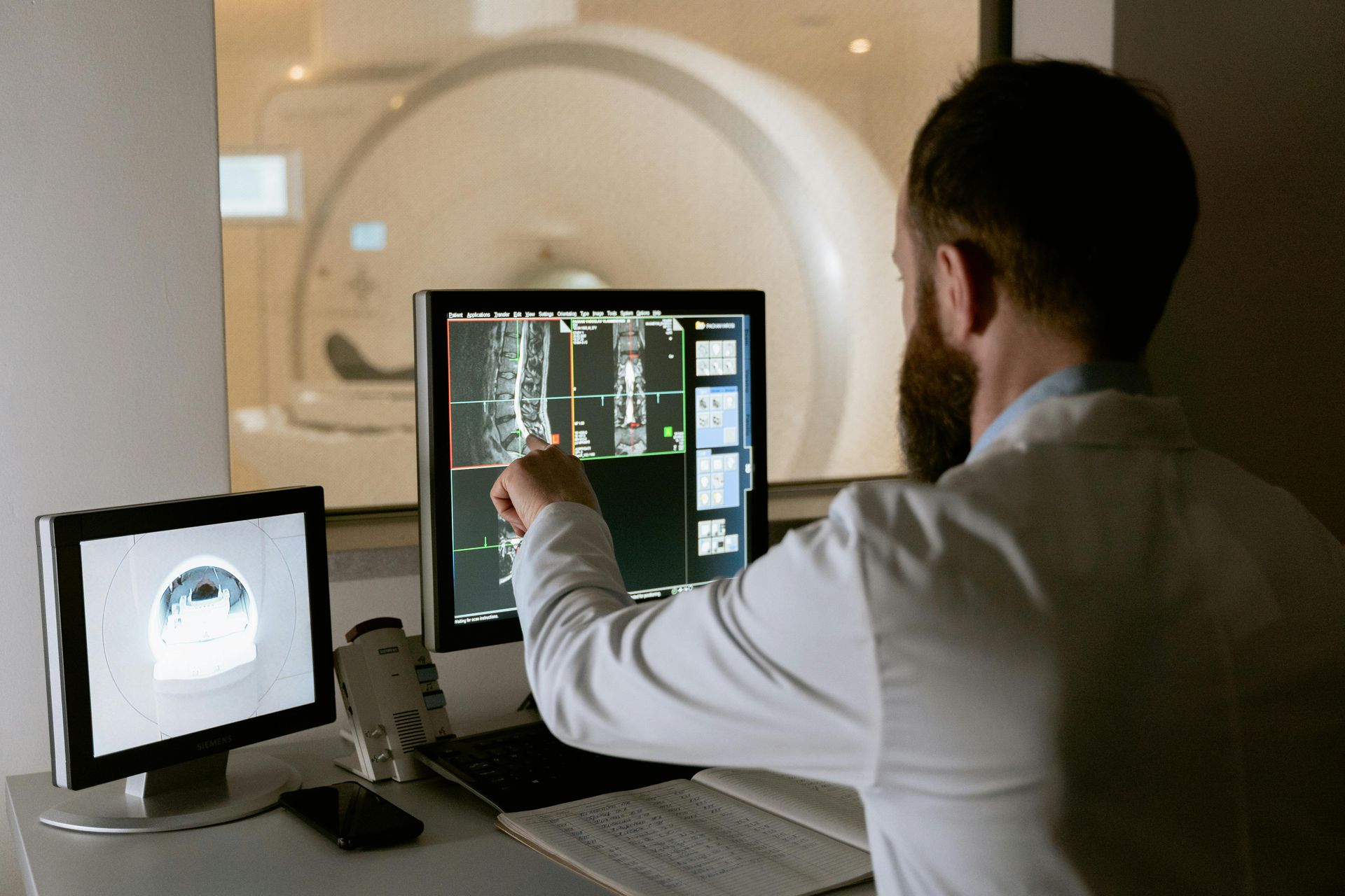 Doctor analyzing an MRI scan on a computer screen, pointing to the image, with the MRI machine visible in the background.
