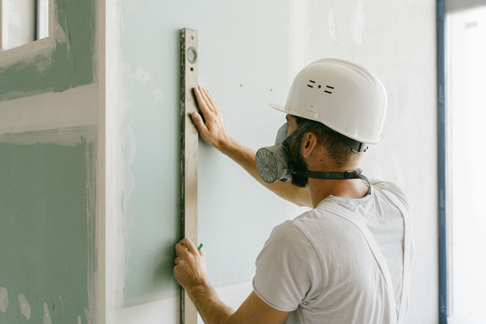 A man wearing a helmet and a gas mask is measuring a wall with a level.