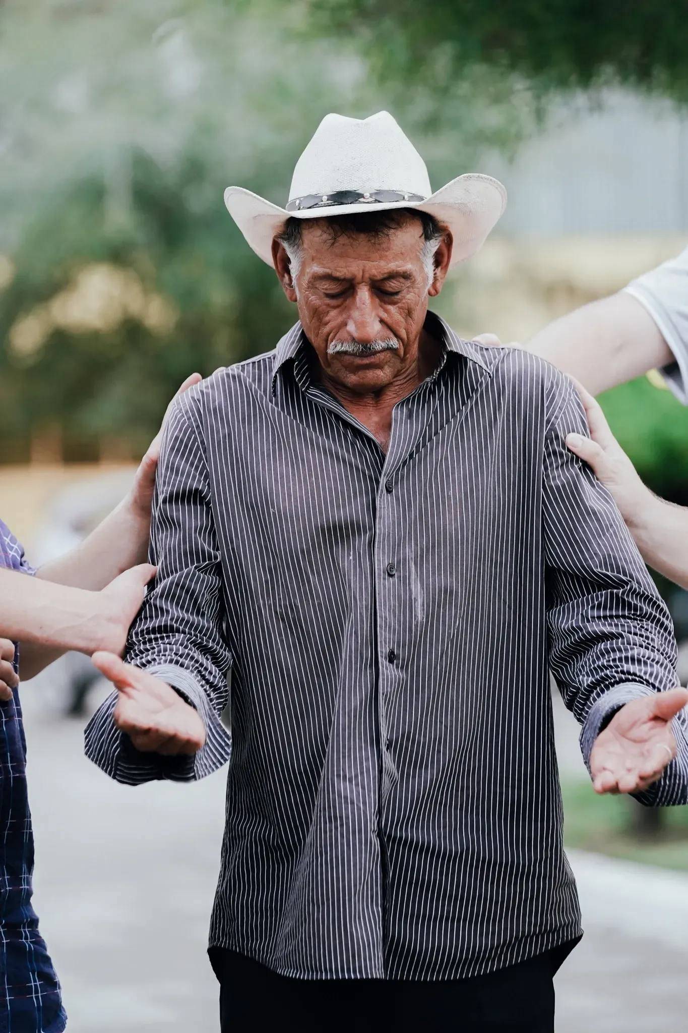 A man in a cowboy hat is praying with his hands outstretched.