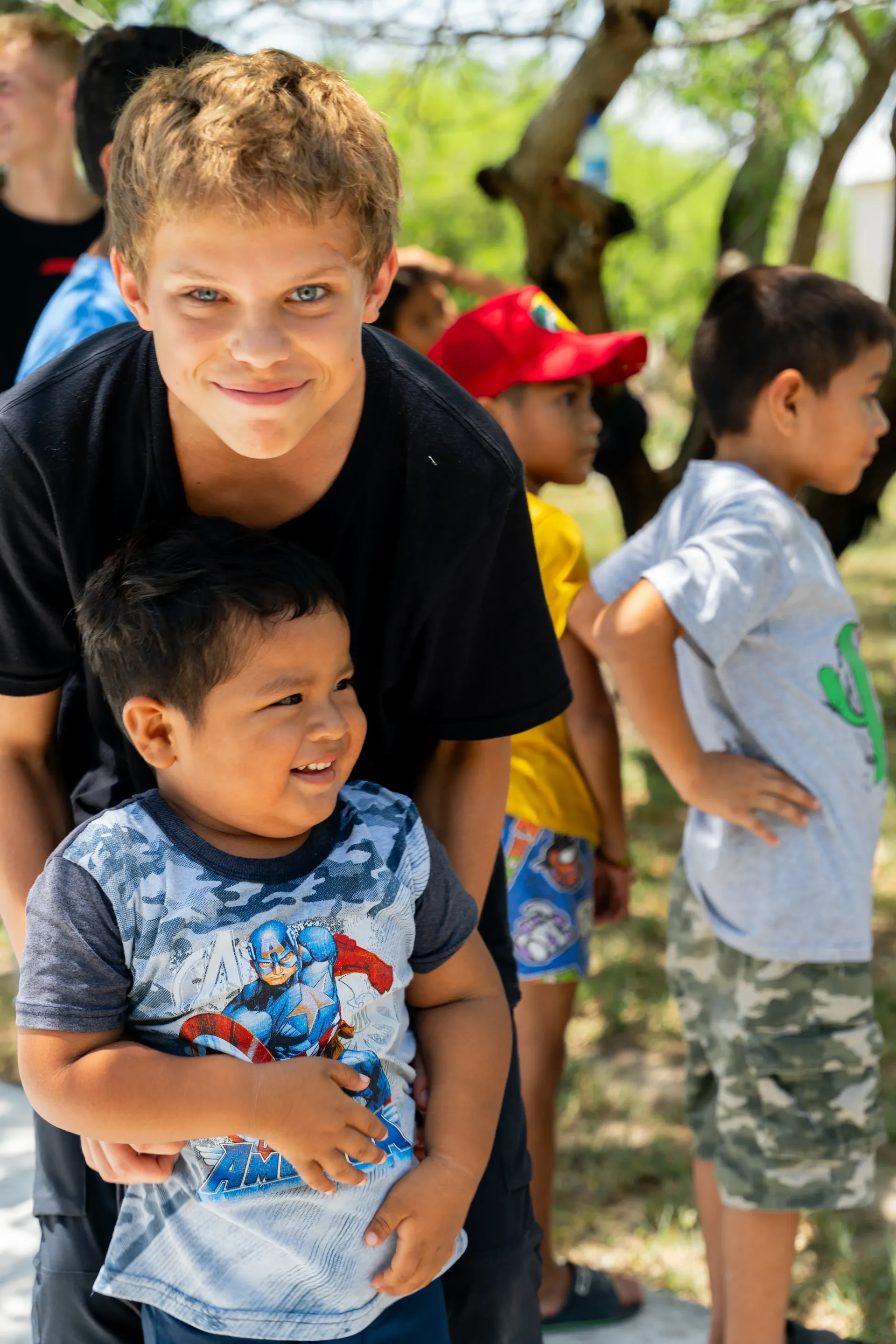 A boy is holding a little boy in his arms in a park.