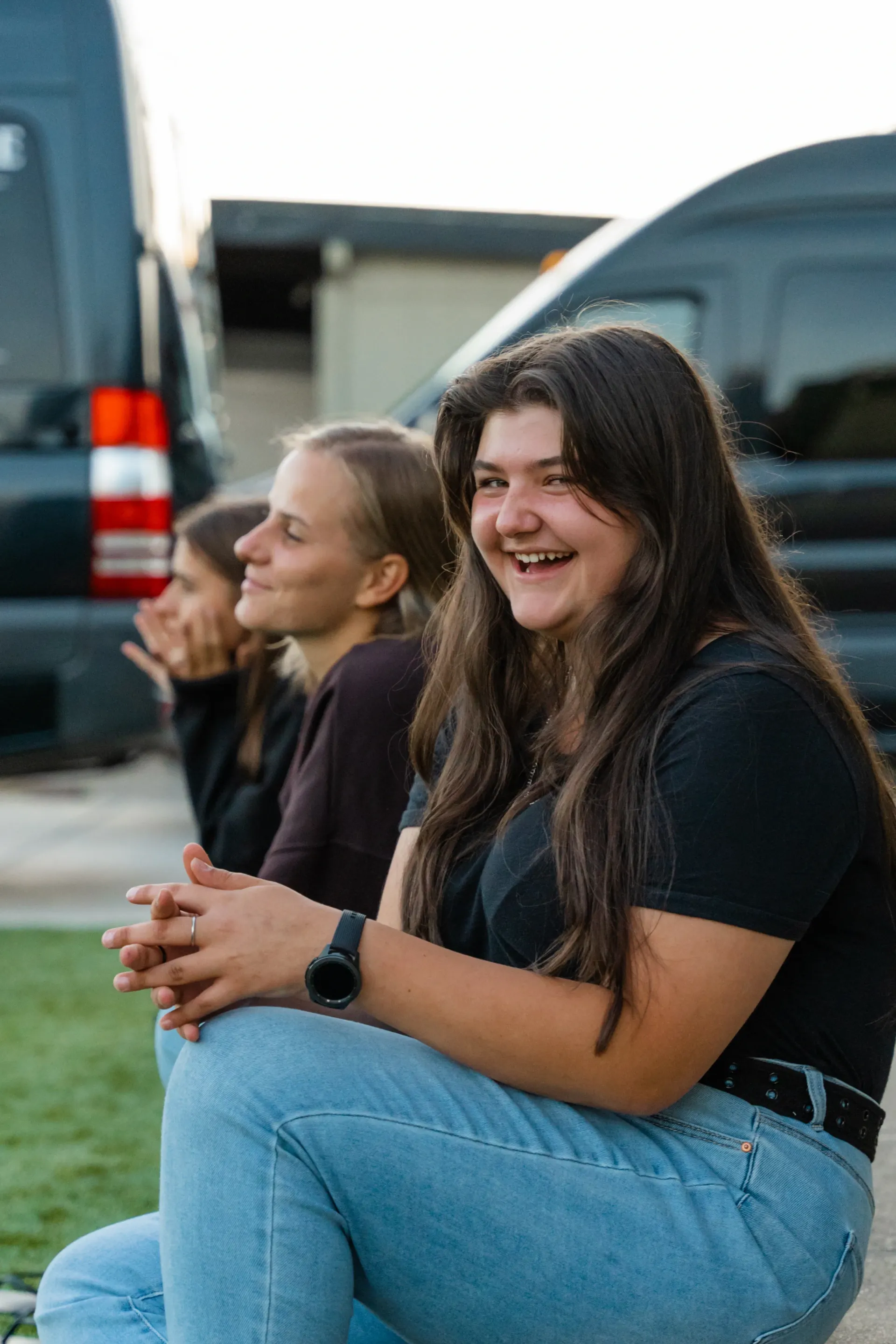 A group of young women are sitting next to each other in front of a van.