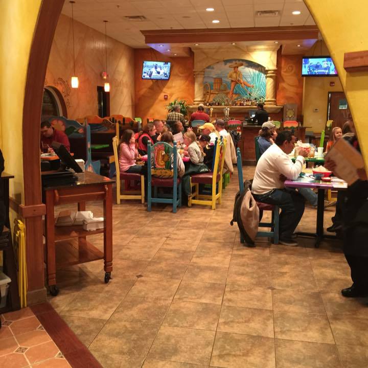A busy Mexican restaurant with customers dining at tables. Colorful chairs, tiled floors, and decorative wall art.