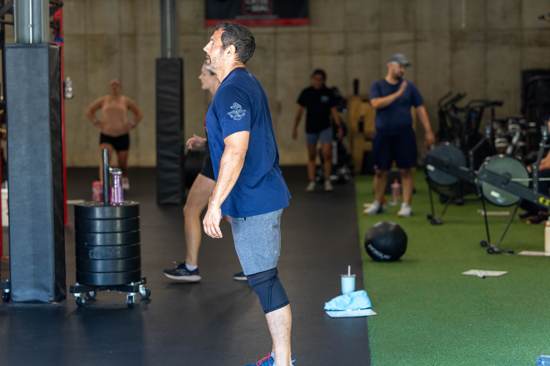 Man in workout gear performing exercise in gym. Others exercise or watch.
