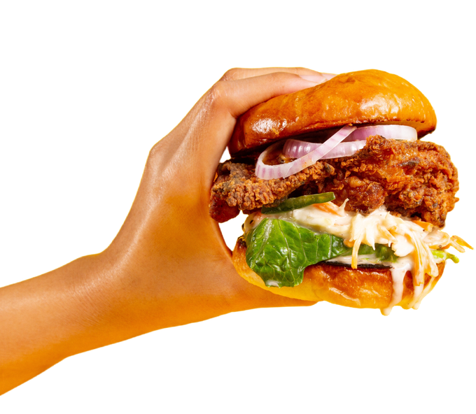 A hand is holding a chicken sandwich with lettuce onions and coleslaw