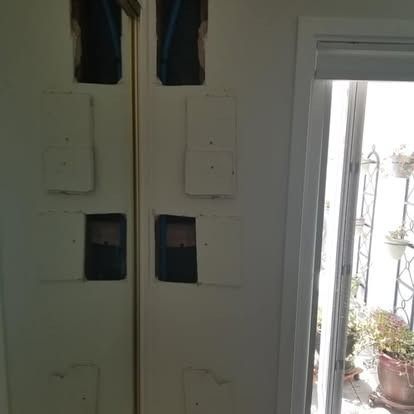White double doors with small windows, partly open to a bright patio with potted plants.
