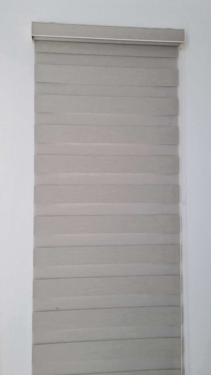 Una persiana gris está colgada en una pared blanca.