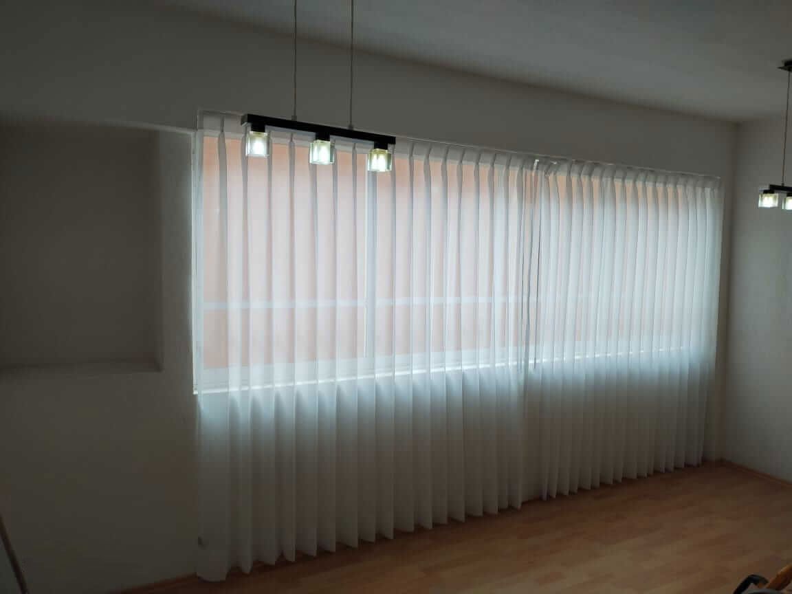 Una sala de estar con una gran ventana y cortinas blancas.
