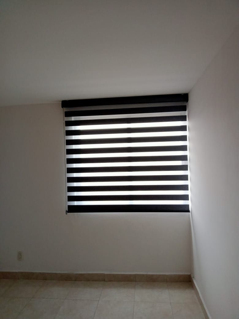 Una habitación con una ventana con una persiana blanca y negra.