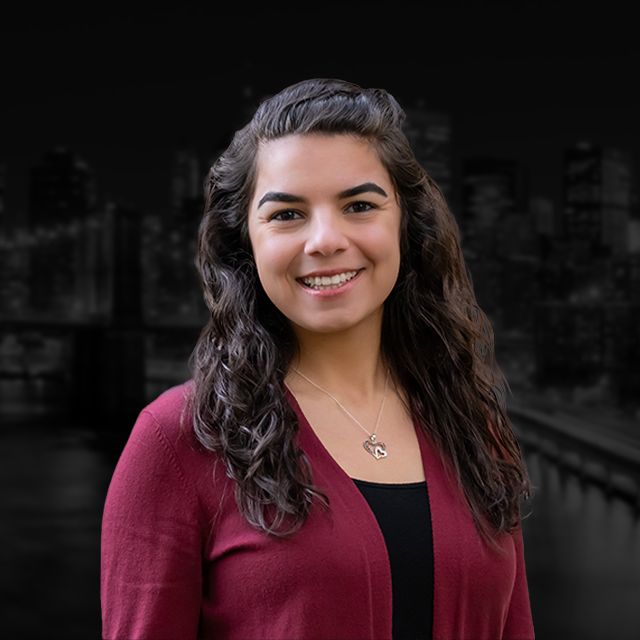A woman wearing a red sweater and a necklace is smiling for the camera.