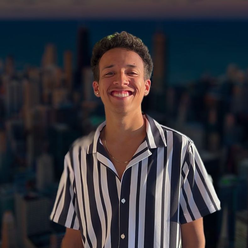 A young man in a striped shirt is smiling in front of a city skyline.