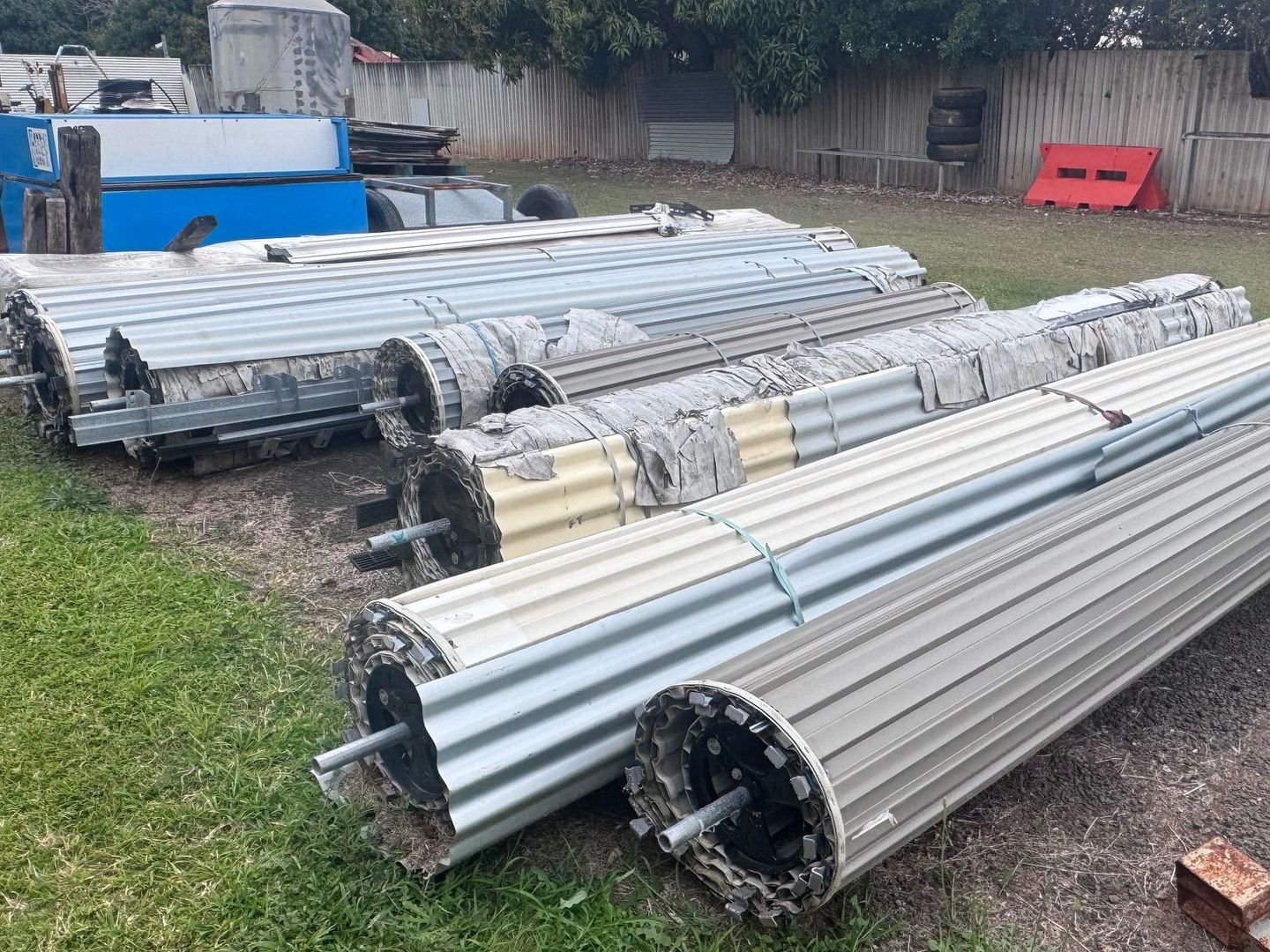 Piles of Rolled-Up Metal Shutters on Grass — Bundaberg Auction Centre in Gooburrum, QLD