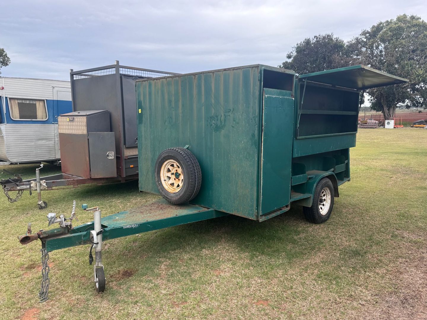 Green Box Trailer with Open Hatch and Spare Tire in A Grassy Area — Bundaberg Auction Centre in Gooburrum, QLD