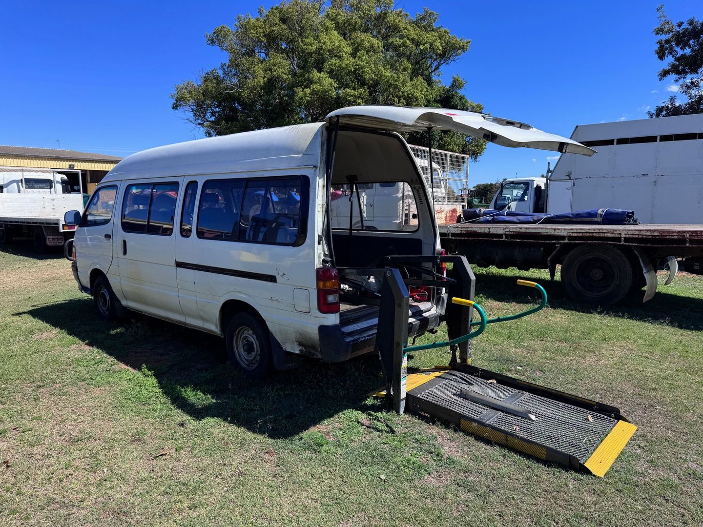 White Van with A Wheelchair Lift Extended on A Grassy Field — Bundaberg Auction Centre in Gooburrum, QLD