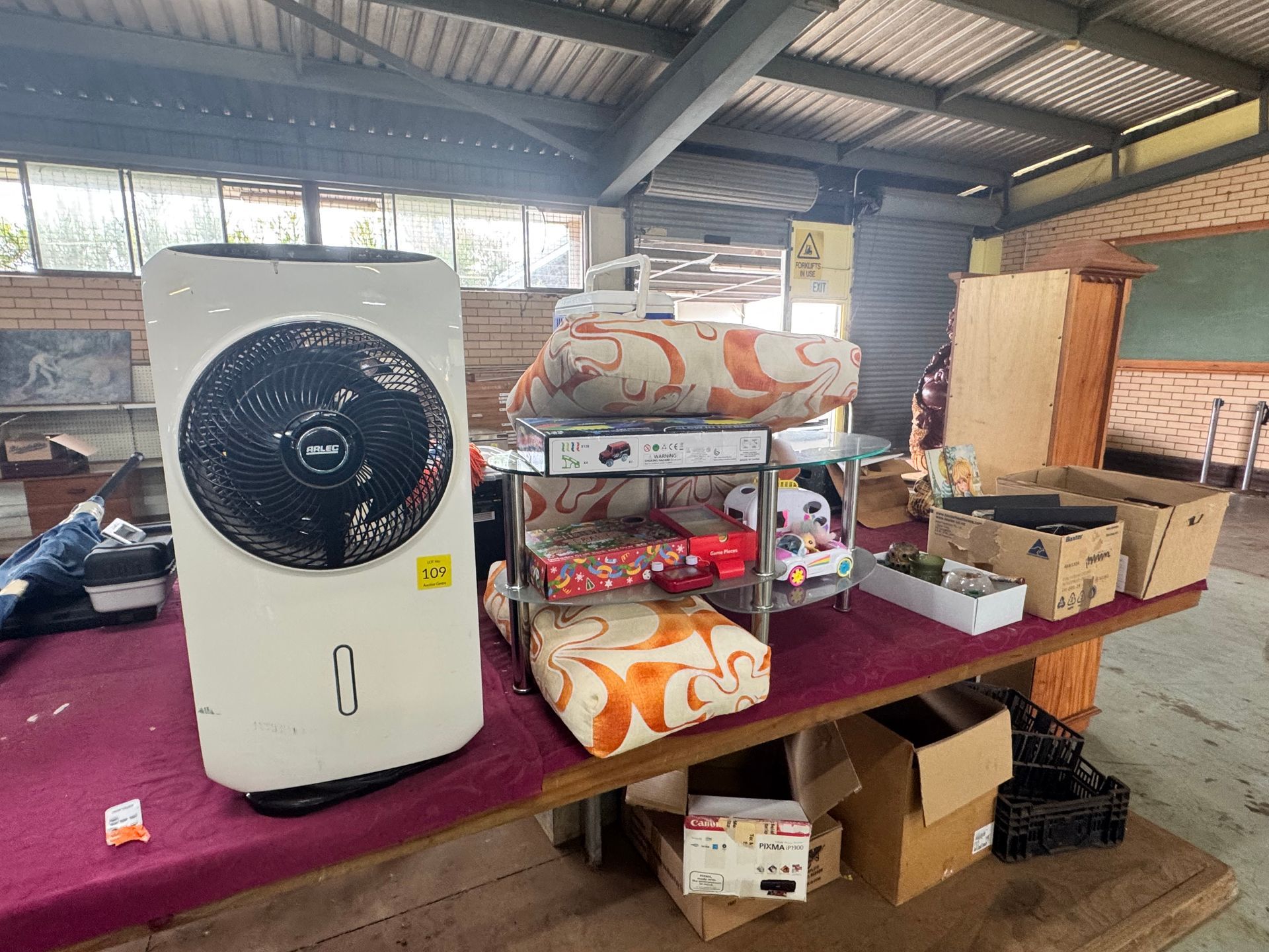 Indoor Garage Sale Setup; Various Items Displayed on A Long Table — Bundaberg Auction Centre in Gooburrum, QLD