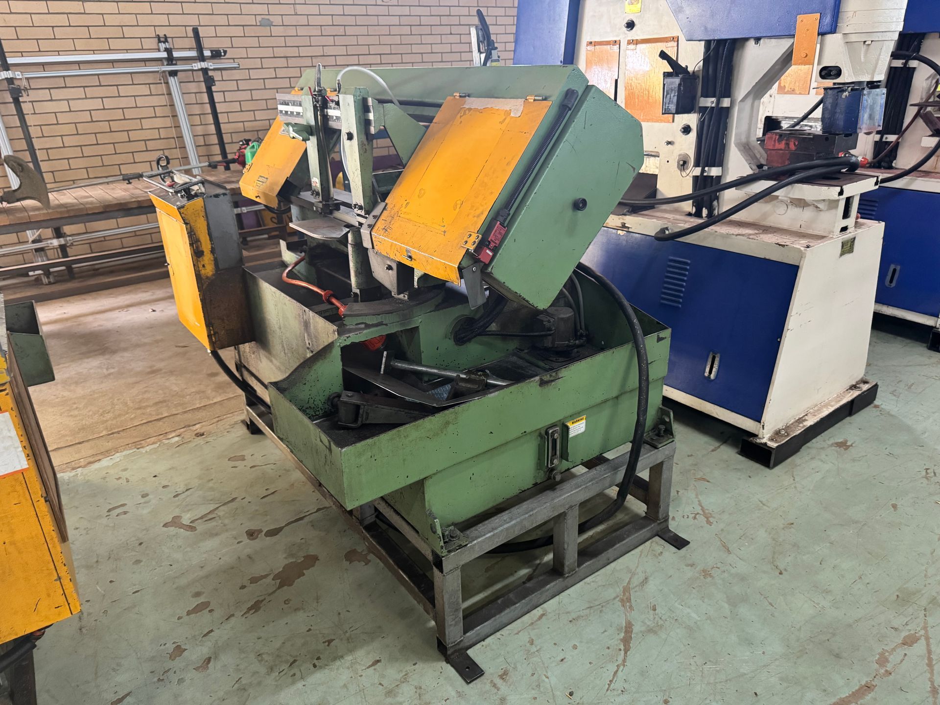 Green Metal Band Saw Machine with Yellow Safety Guards, in A Workshop — Bundaberg Auction Centre in Gooburrum, QLD