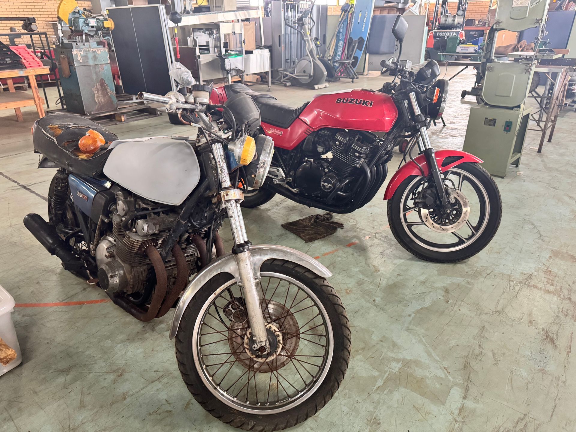 Two Vintage Motorcycles, One Red, One Grey, in A Garage Setting with Tools and Equipment — Bundaberg Auction Centre in Gooburrum, QLD