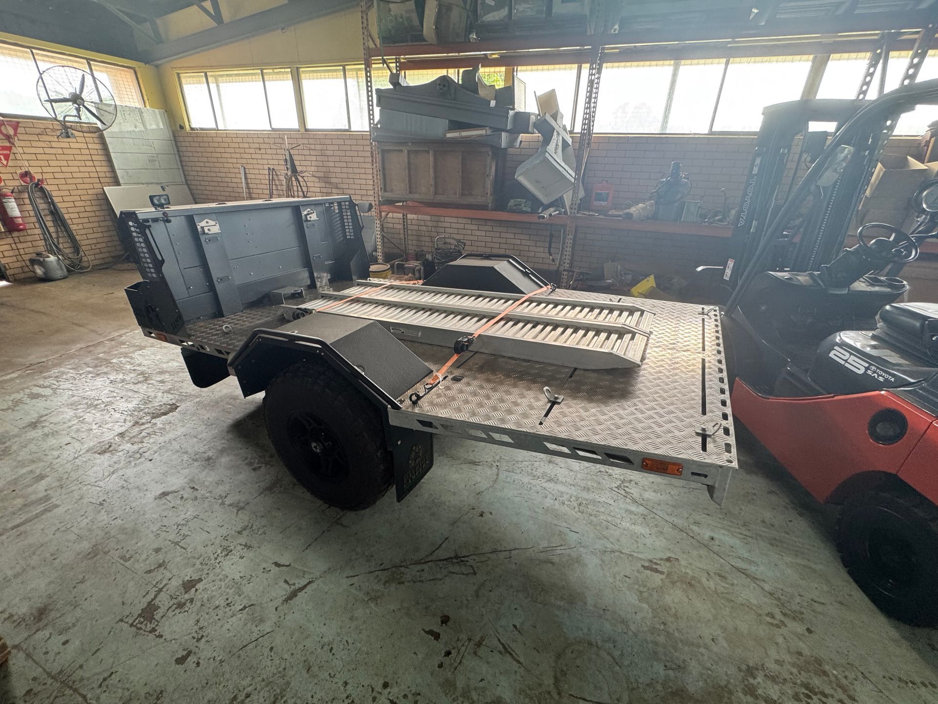 A Gray Trailer with A Textured Metal Bed Sits on A Concrete Floor Next to A Forklift — Bundaberg Auction Centre in Gooburrum, QLD