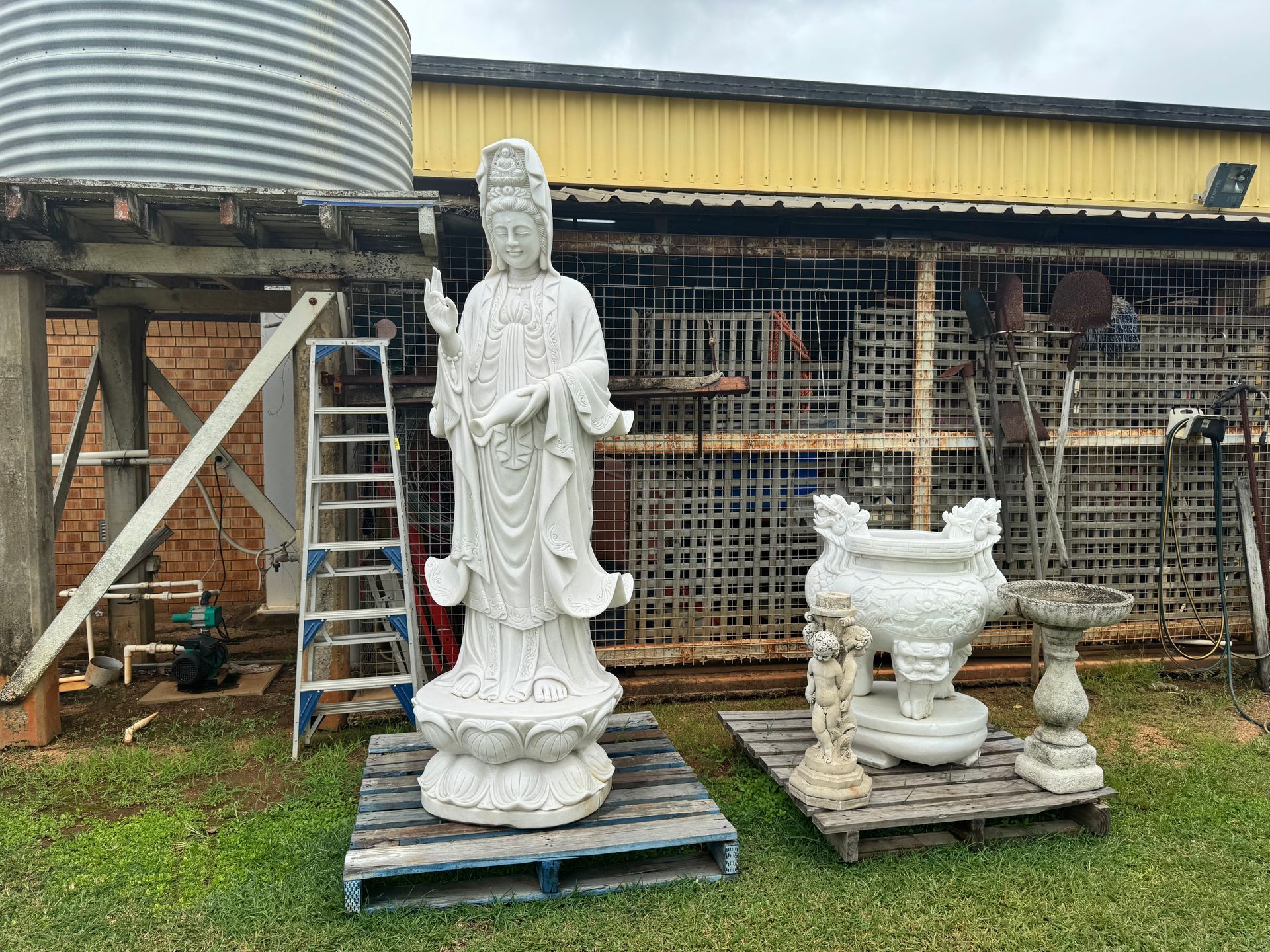 White Statue of A Deity, Vase, and Pedestal on Pallets in Front of A Building with A Water Tank — Bundaberg Auction Centre in Gooburrum, QLD