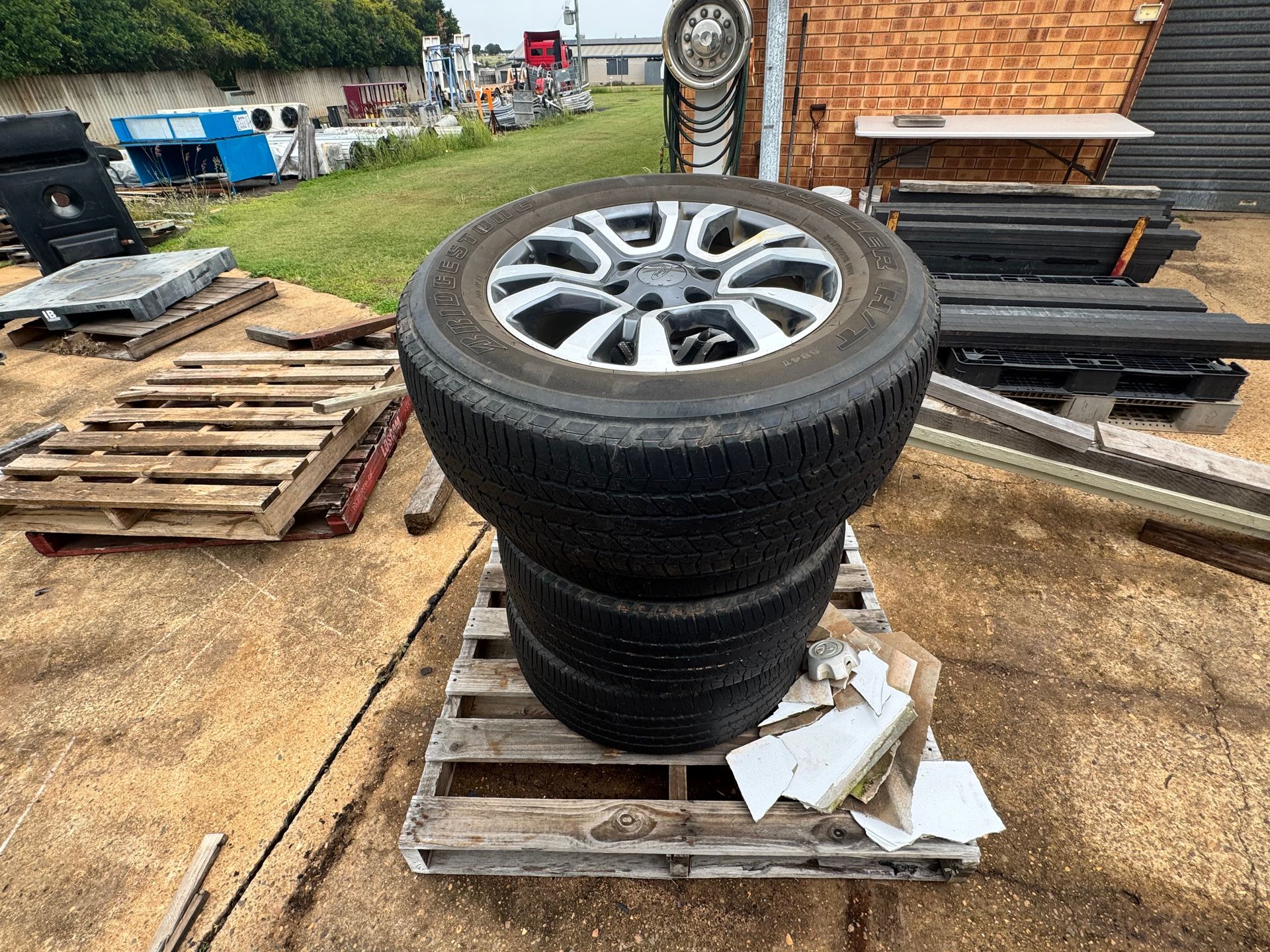Four Tires Stacked on A Wooden Pallet Outdoors Near Various Car Parts and A Brick Wall — Bundaberg Auction Centre in Gooburrum, QLD