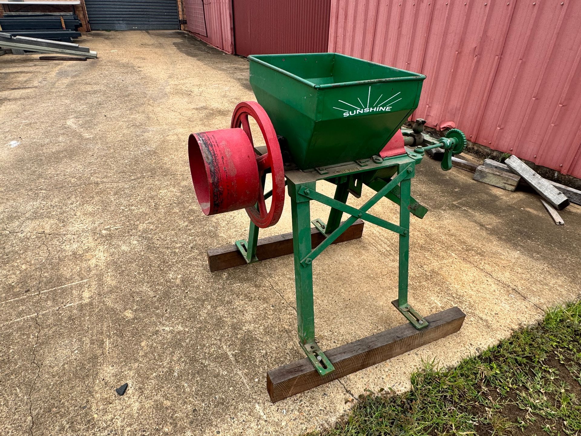 Green and Red Grain Grinder on A Concrete Surface, with A Red Metal Wheel and Green Hopper — Bundaberg Auction Centre in Gooburrum, QLD
