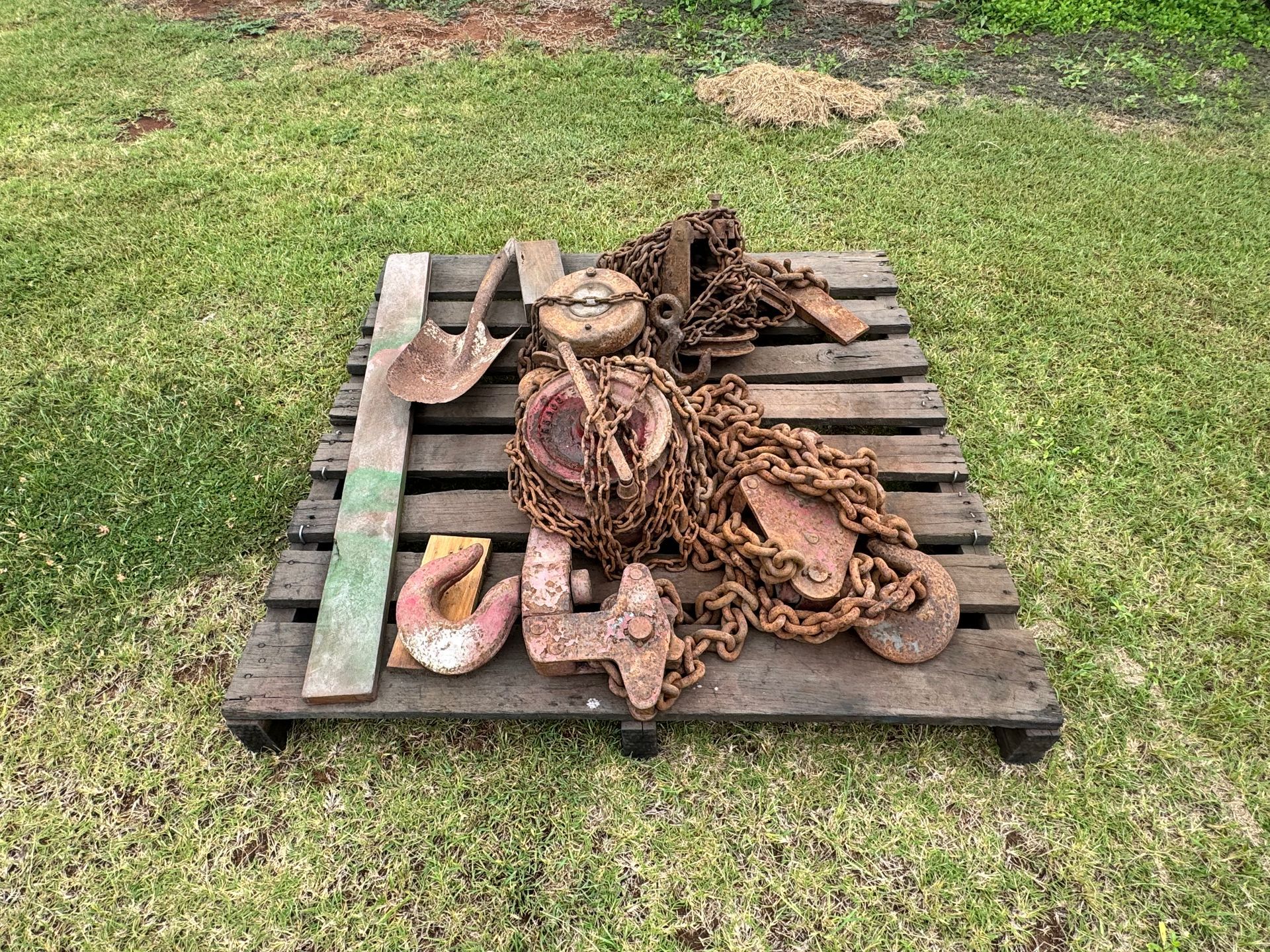 Rusty Metal Chains, Pulleys, and Hooks on A Wooden Pallet in A Grassy Outdoor Setting — Bundaberg Auction Centre in Gooburrum, QLD