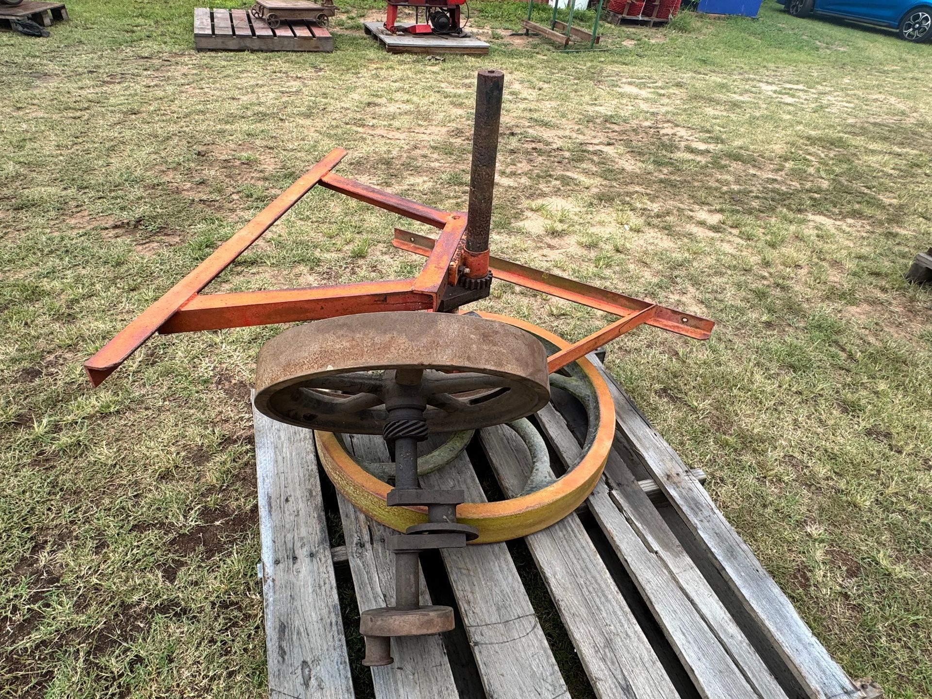 Rusty Metal Farm Implement on Wooden Pallet, Outdoors. Orange and Yellow Paint — Bundaberg Auction Centre in Gooburrum, QLD