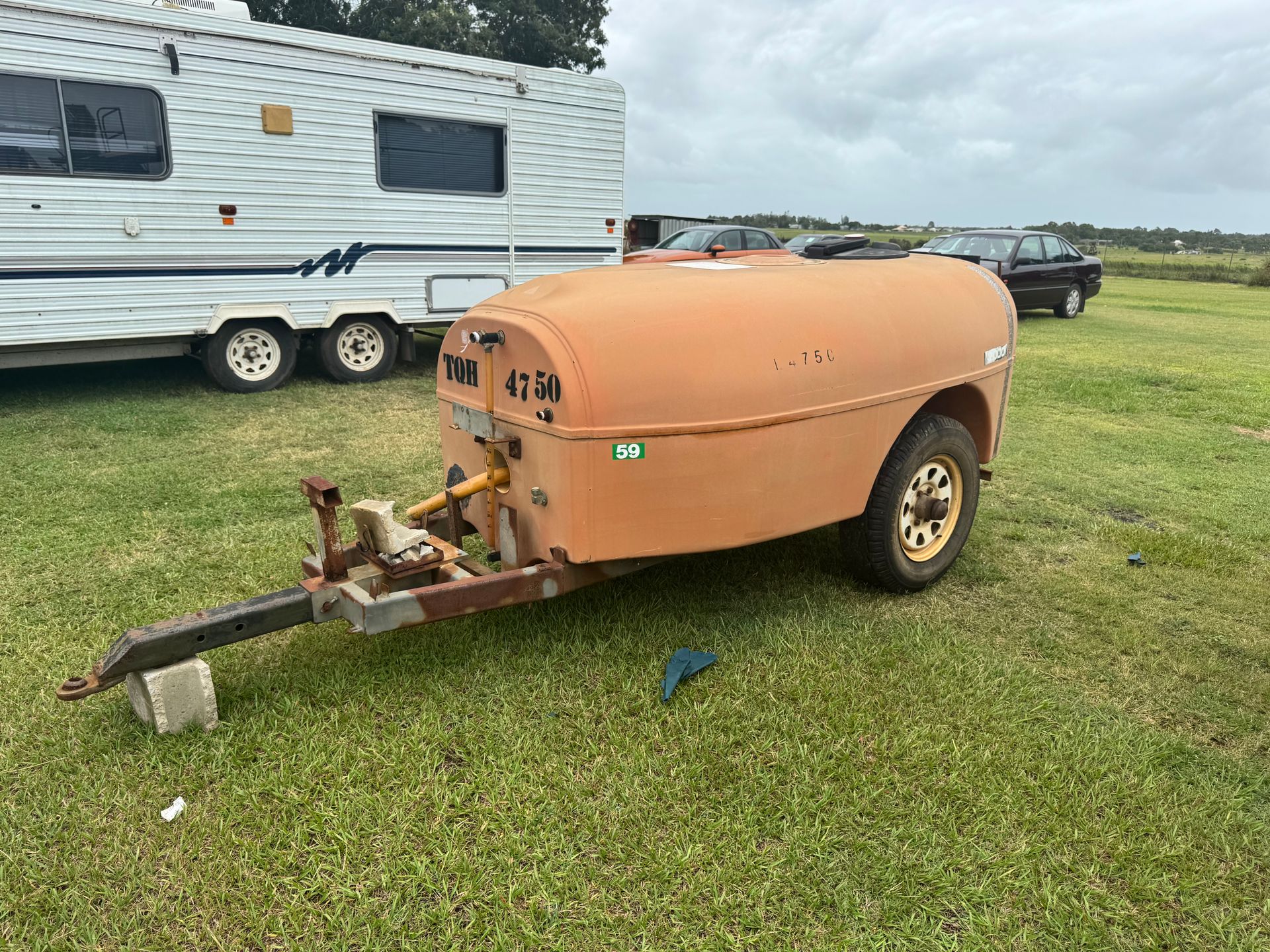 Orange Trailer with Rounded Top, Hitch, and Single Wheel in Grassy Field with Rv and Car in Background — Bundaberg Auction Centre in Gooburrum, QLD