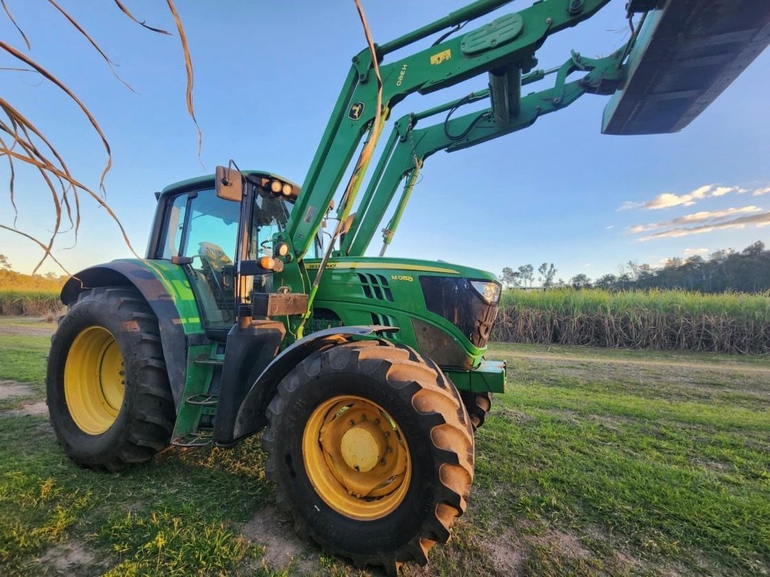 A red tractor with a bucket attached to it is parked in front of a shed.