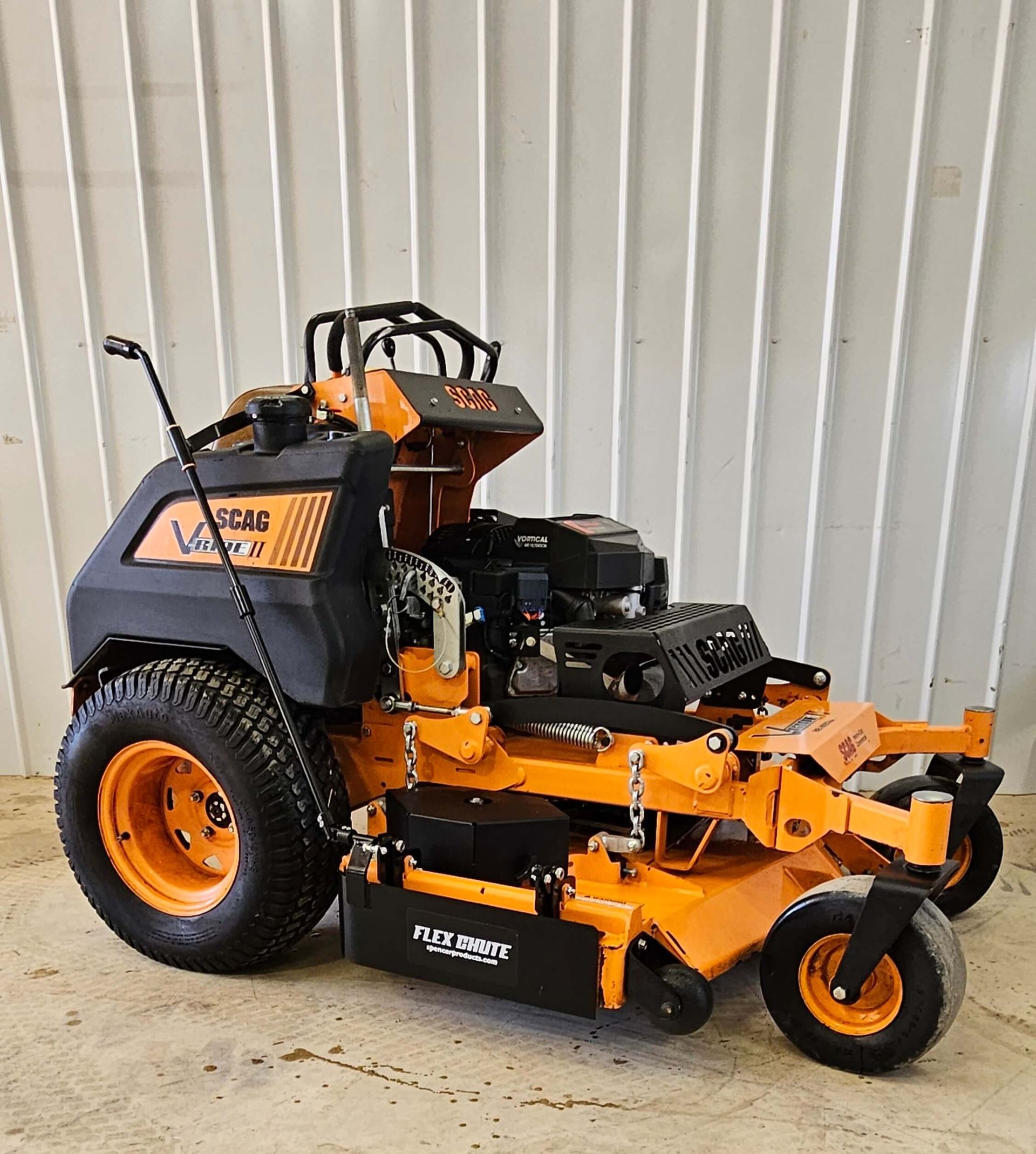 An orange and black lawn mower is parked in front of a white wall.