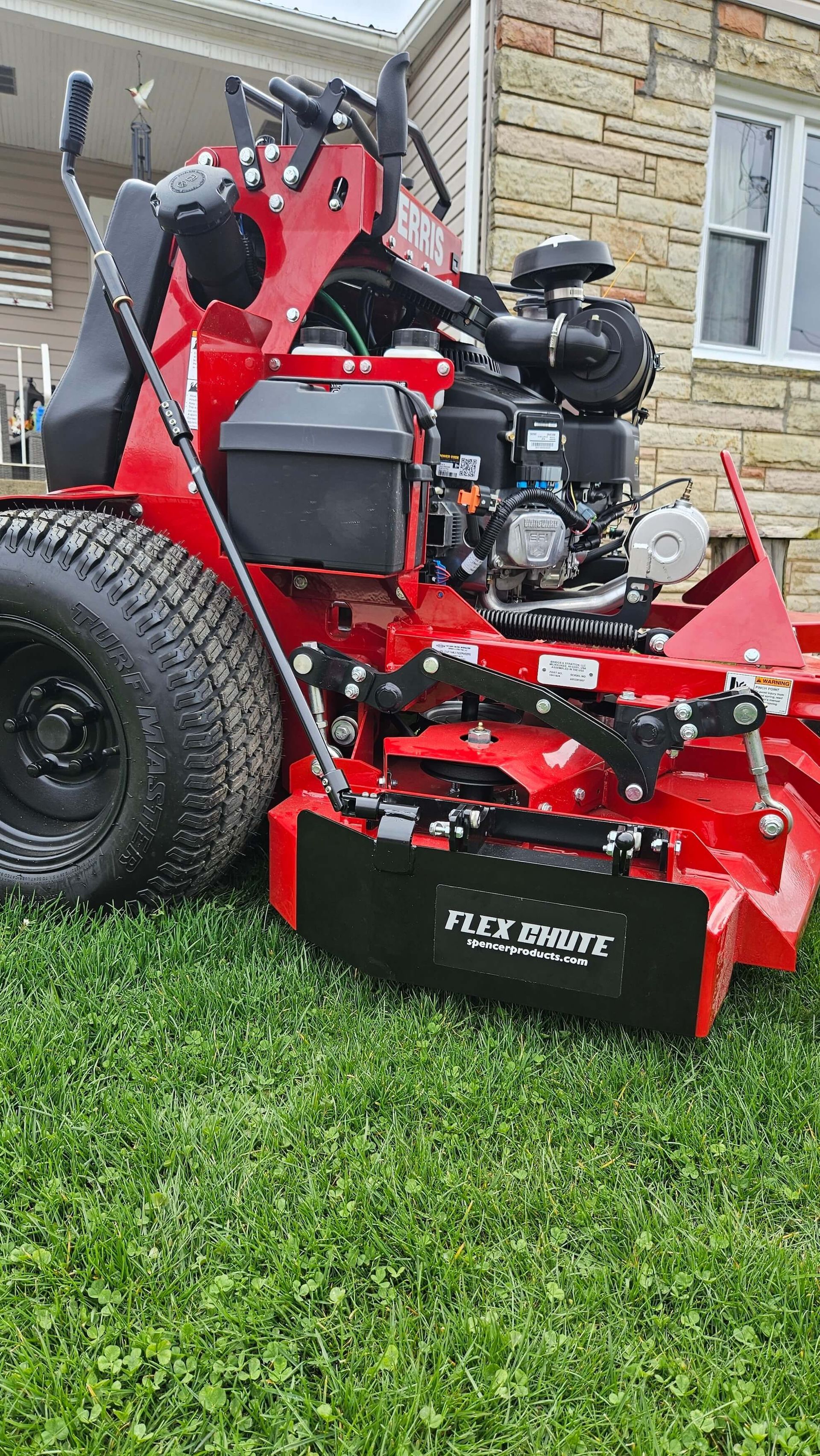 A red lawn mower is parked in the grass in front of a house.