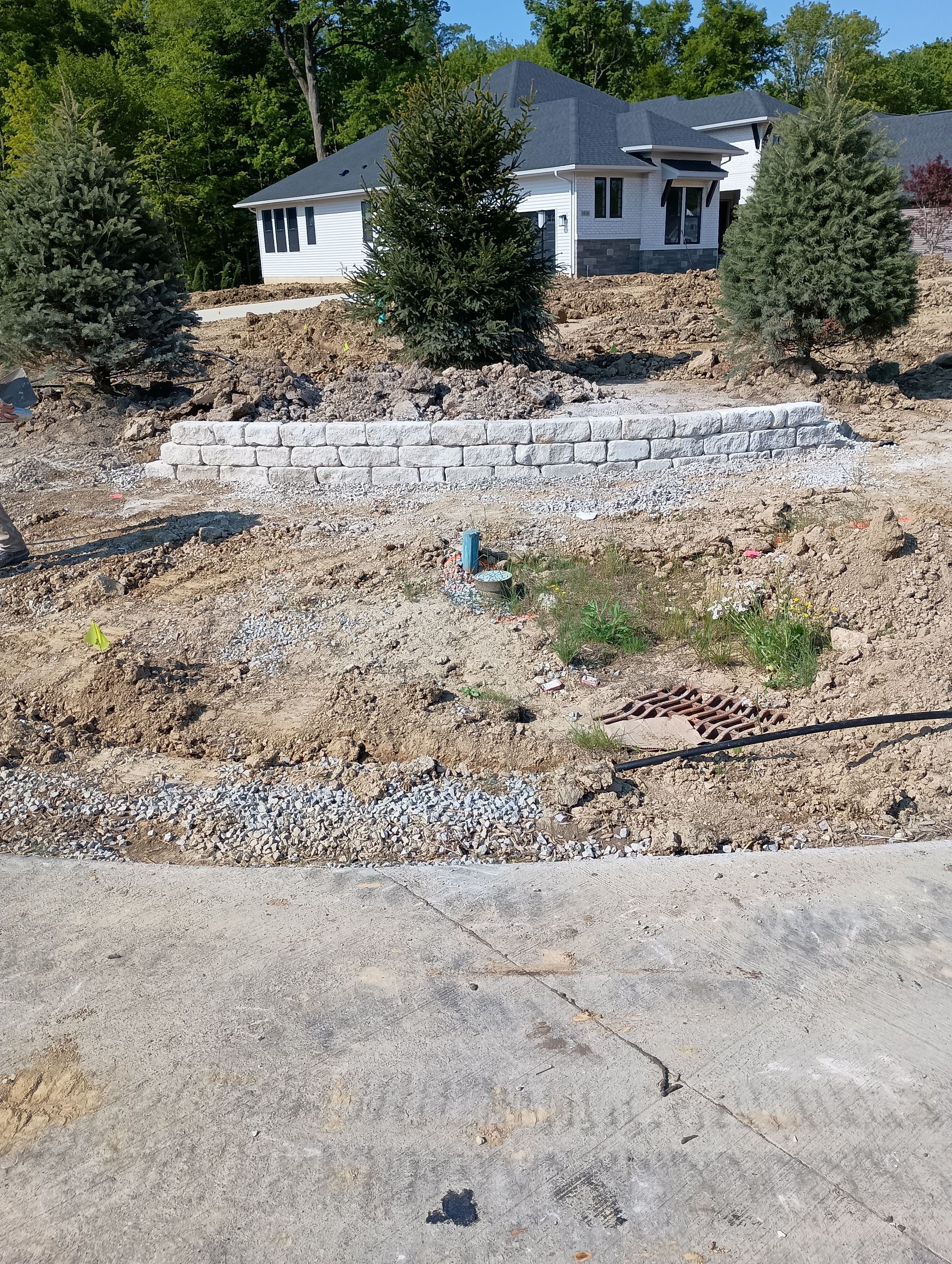 Construction site: retaining wall in front of a white house with a dark roof.