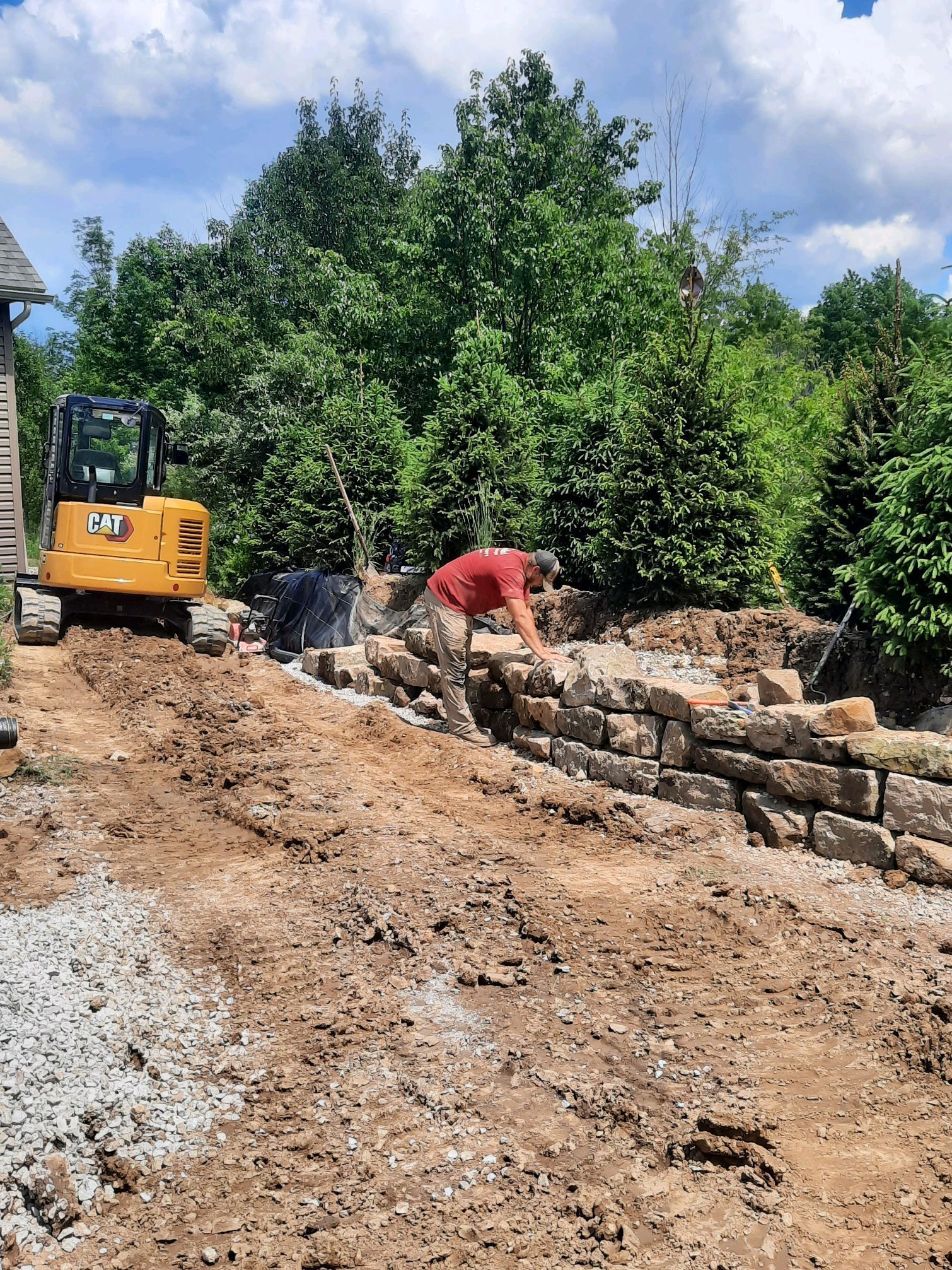 Man building stone retaining wall with an excavator on a sunny day.