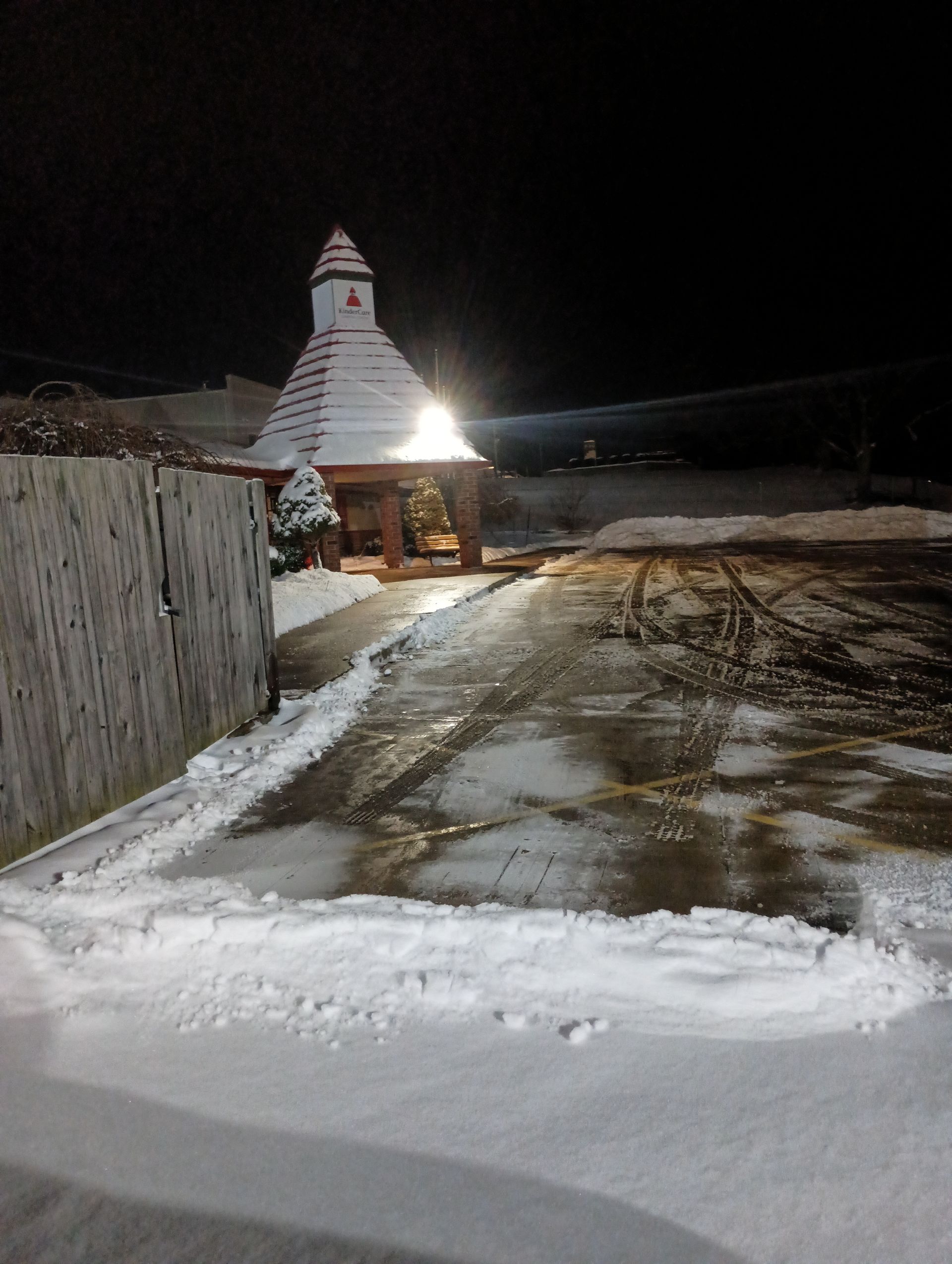 Snowy night scene with a building under bright light, featuring a unique peaked roof.