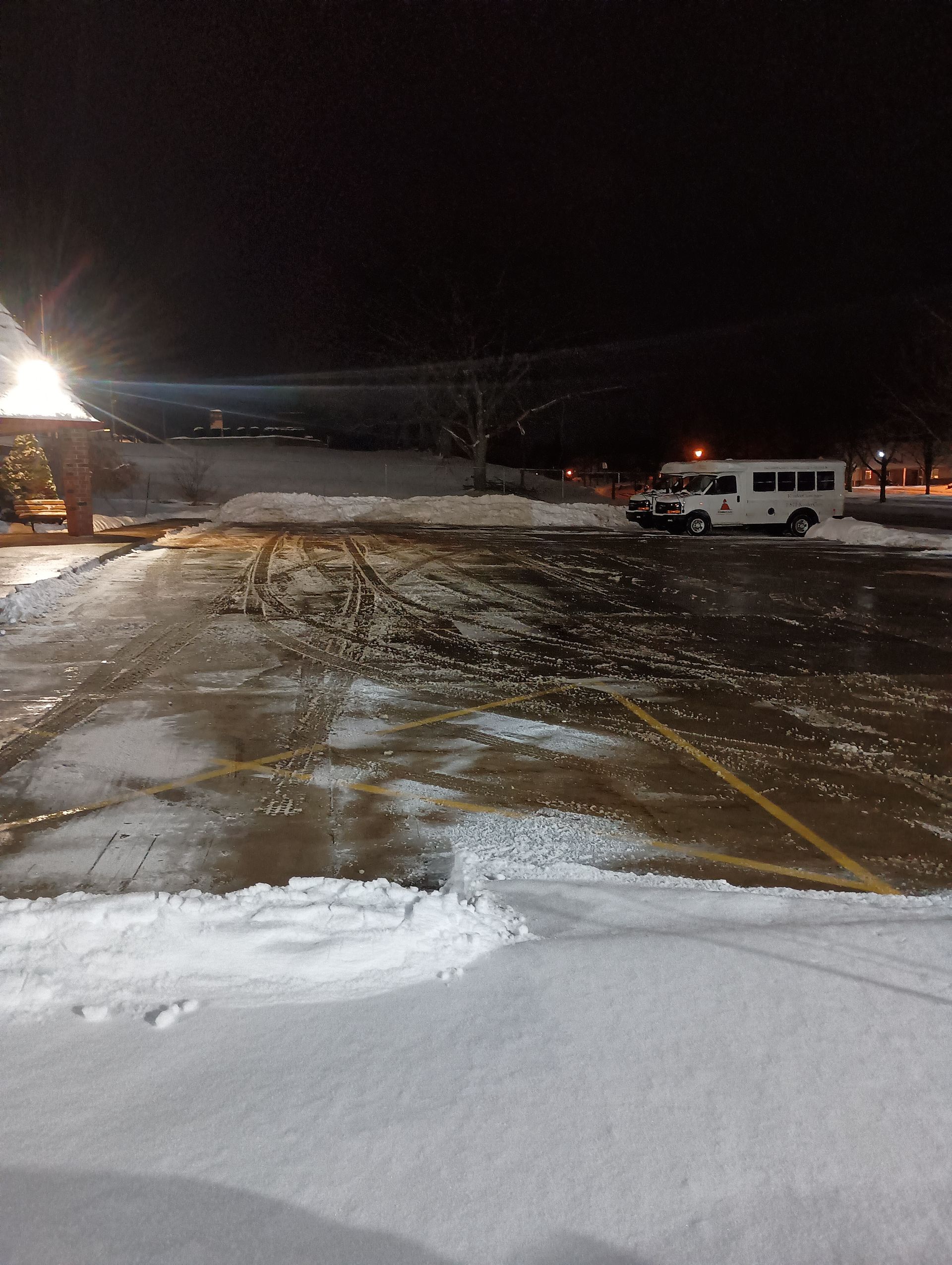 Snowy parking lot at night; a bus parked nearby, snow piles, and icy patches.