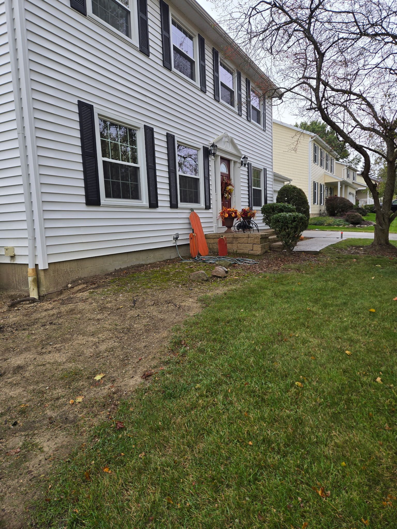 White two-story house with black shutters, fall decorations on the porch, and grass lawn in front.